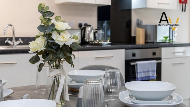 A modern kitchen with white cabinets, a stainless steel sink, and a vase with white flowers on the counter.