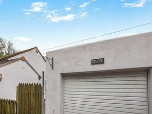 Un edificio con puerta de garaje, un letrero de metal que dice 'SPRUCE' y una valla de madera.