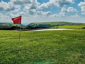 Un parcours de golf avec un drapeau rouge, une pelouse verdoyante et luxuriante, et des collines douces en arrière-plan.