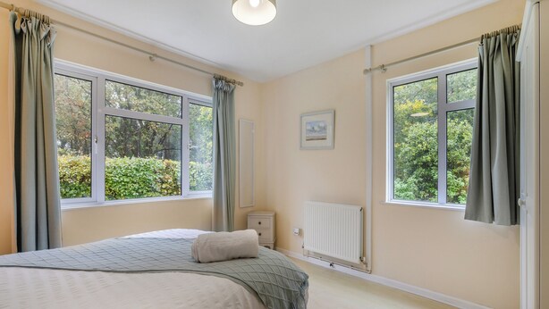 A bedroom with a bed, two windows, a radiator, and a picture on the wall. - Spruce Cottage - UK46875 (Hartland)