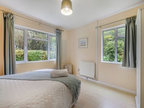 Un dormitorio con una cama, dos ventanas, un radiador y un cuadro en la pared.