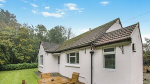 A white house with a tiled roof, a small garden, and a wooden table with chairs. - Spruce Cottage - UK46875 (Hartland)