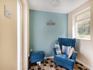 A room with a blue armchair, a small ottoman, a wall-mounted sign, and a window with a view of trees.