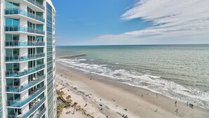 A high-rise hotel with multiple balconies overlooking a beach and ocean. - Condos at Sandy Beach by Beach Trips  (Myrtle Beach)