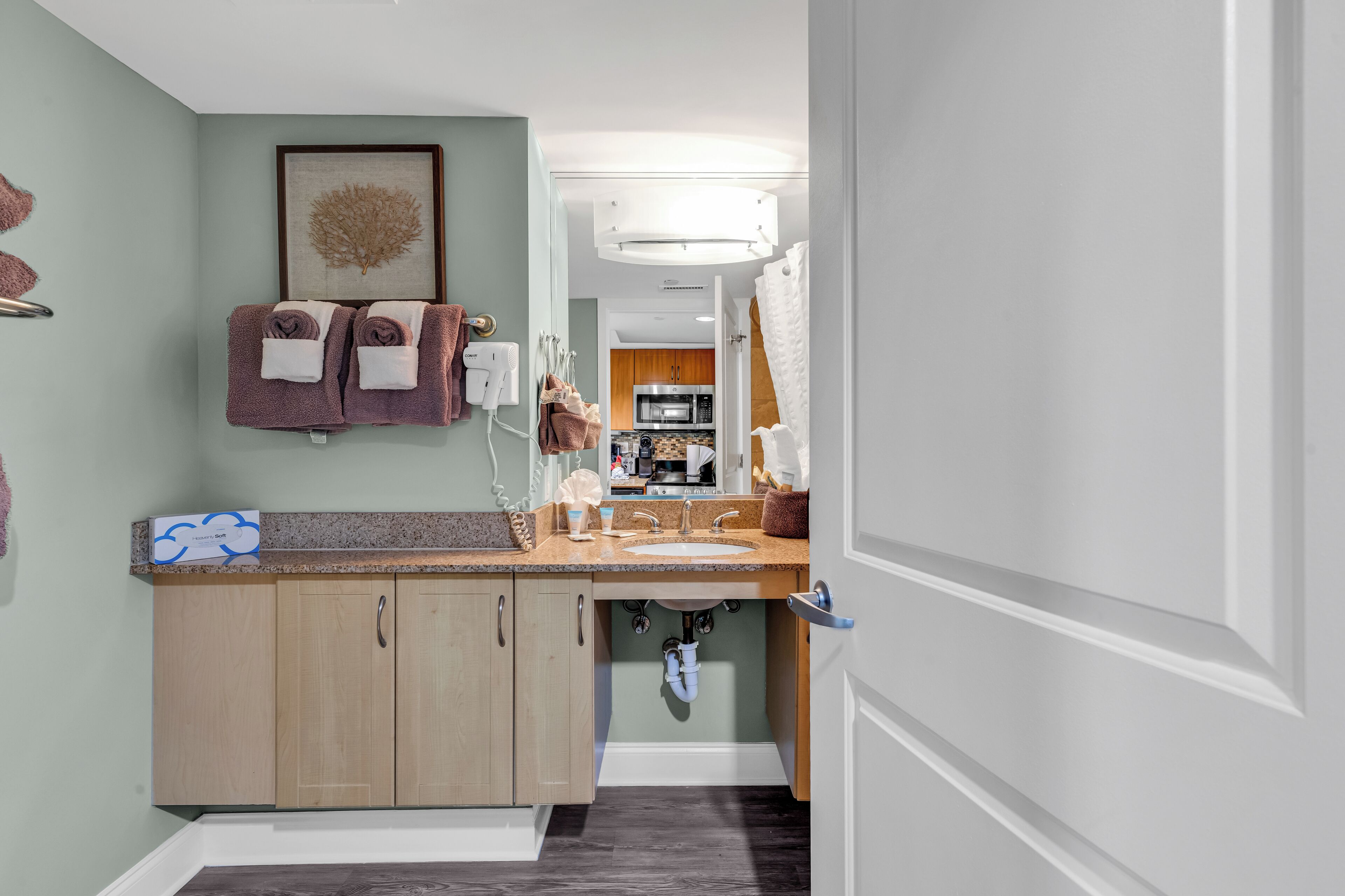 A modern bathroom with a sink, countertop, and wooden cabinets. There is a framed artwork on the wall and towels hanging on a rack.