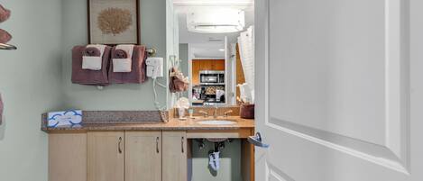 A modern bathroom with a sink, countertop, and wooden cabinets. There is a framed artwork on the wall and towels hanging on a rack.