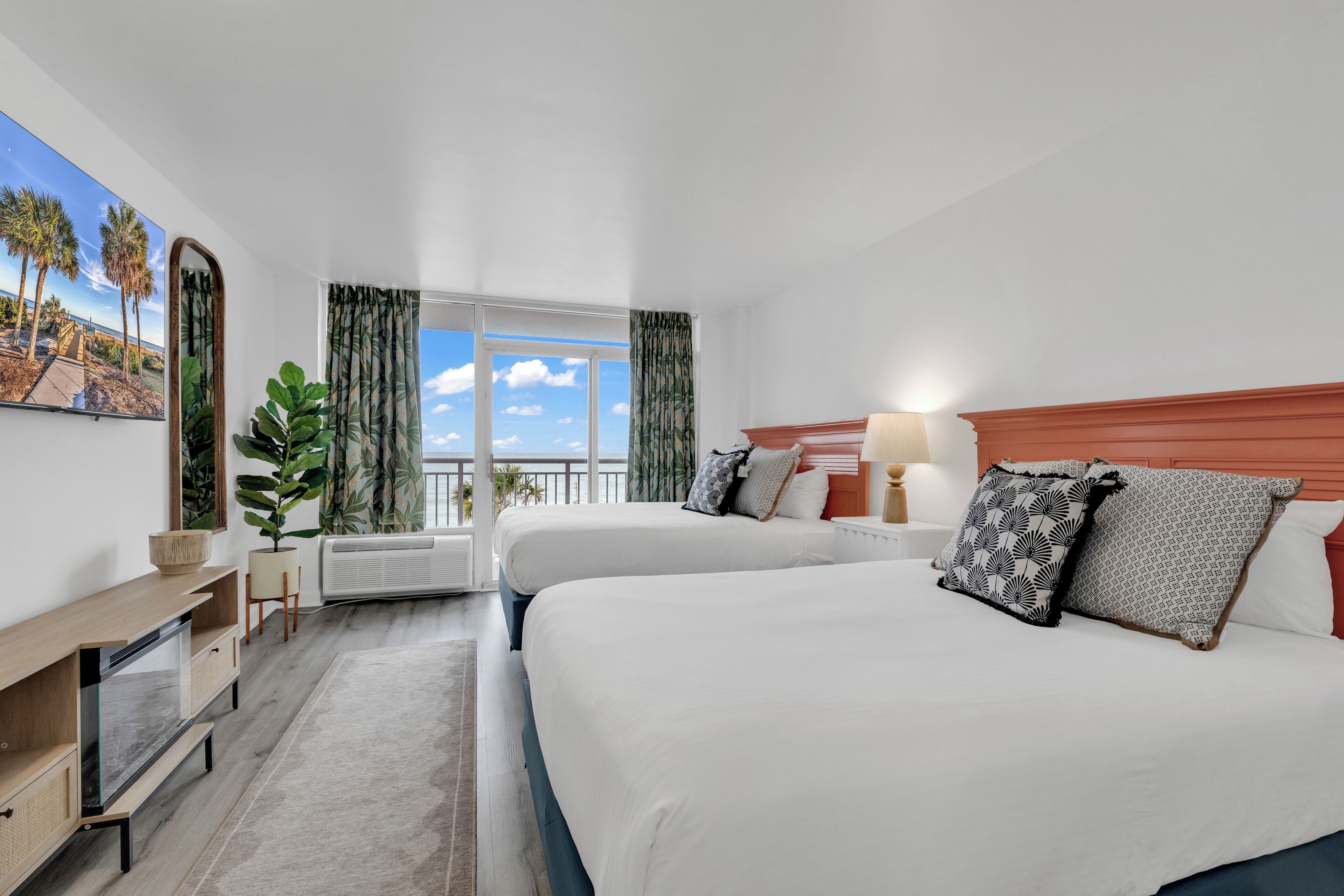 Une chambre d’hôtel avec deux lits, une grande fenêtre donnant sur un beau paysage, un bureau et une plante.
