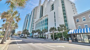 A modern hotel with multiple floors, a flat facade, and a blue and white striped awning. - Condos at Sandy Beach by Beach Trips  (Myrtle Beach)
