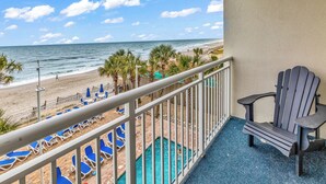 A balcony with a view of the beach, a pool, and a chair. - Condos at Sandy Beach by Beach Trips  (Myrtle Beach)