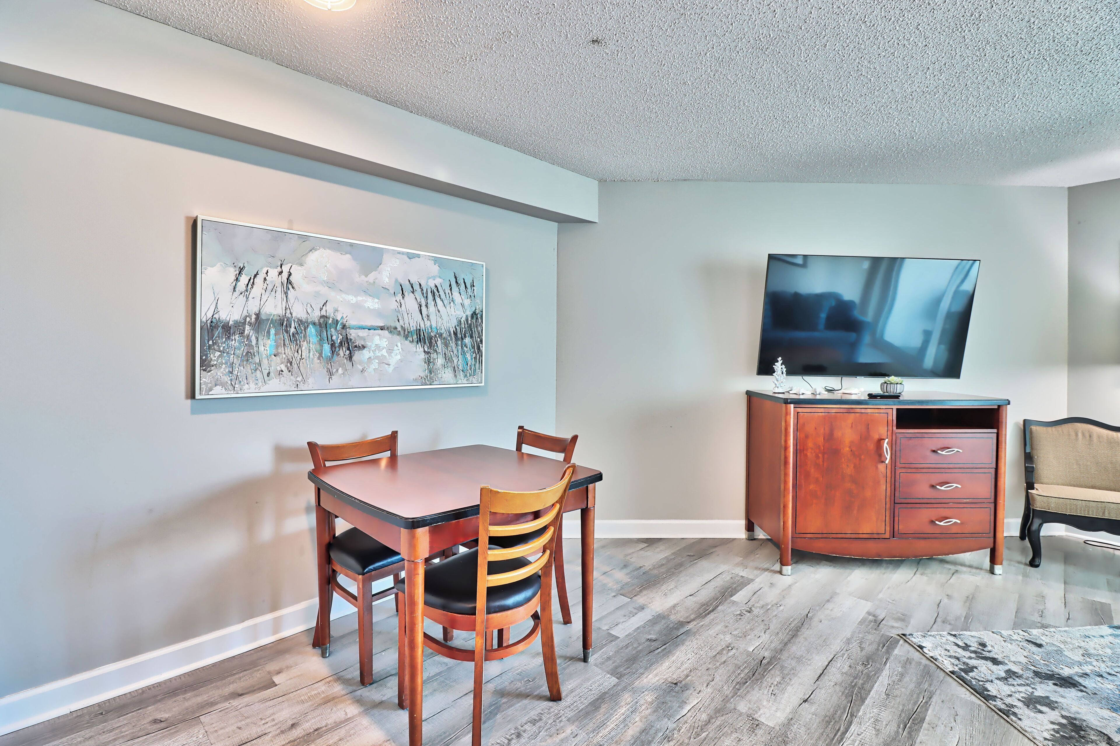A dining area with a wooden table and chairs, a cabinet with drawers, and a flat-screen TV mounted on the wall.
