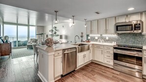 A modern kitchen with stainless steel appliances, a large island, and a view to the outside. - Condos at Sandy Beach by Beach Trips  (Myrtle Beach)