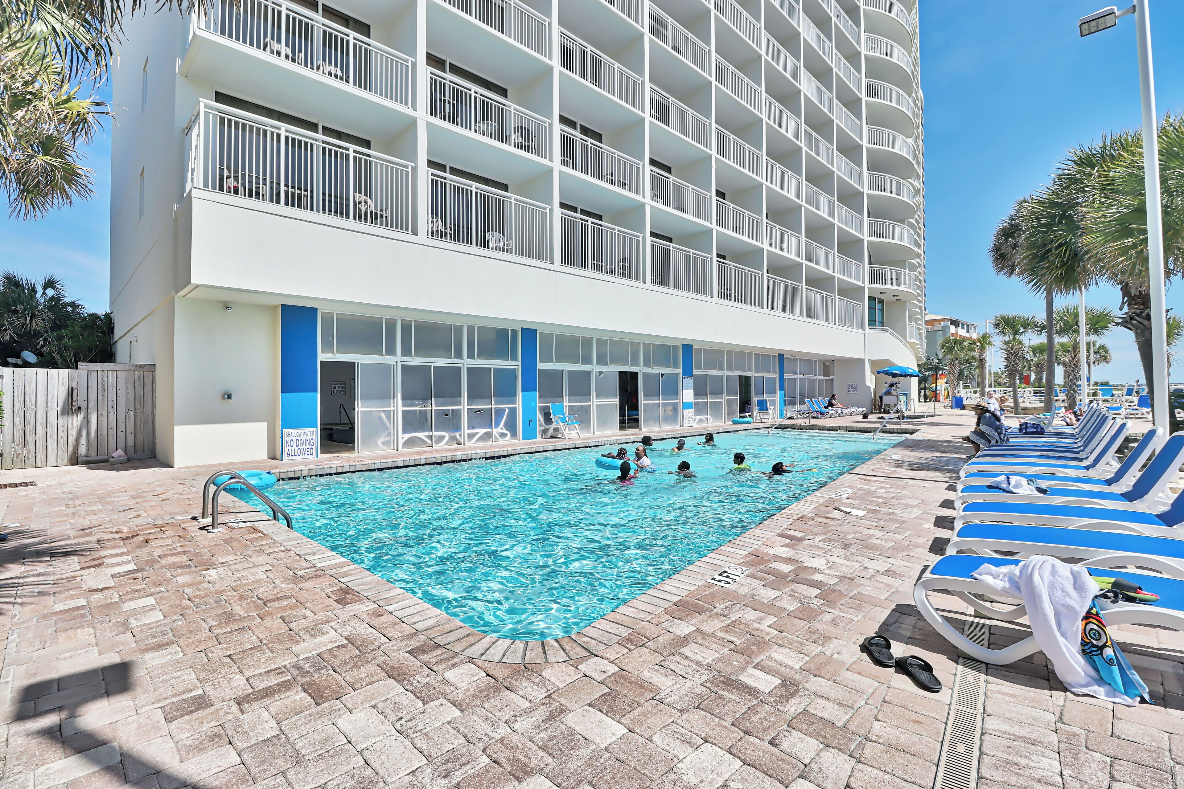 A swimming pool area with lounge chairs and a building with balconies.