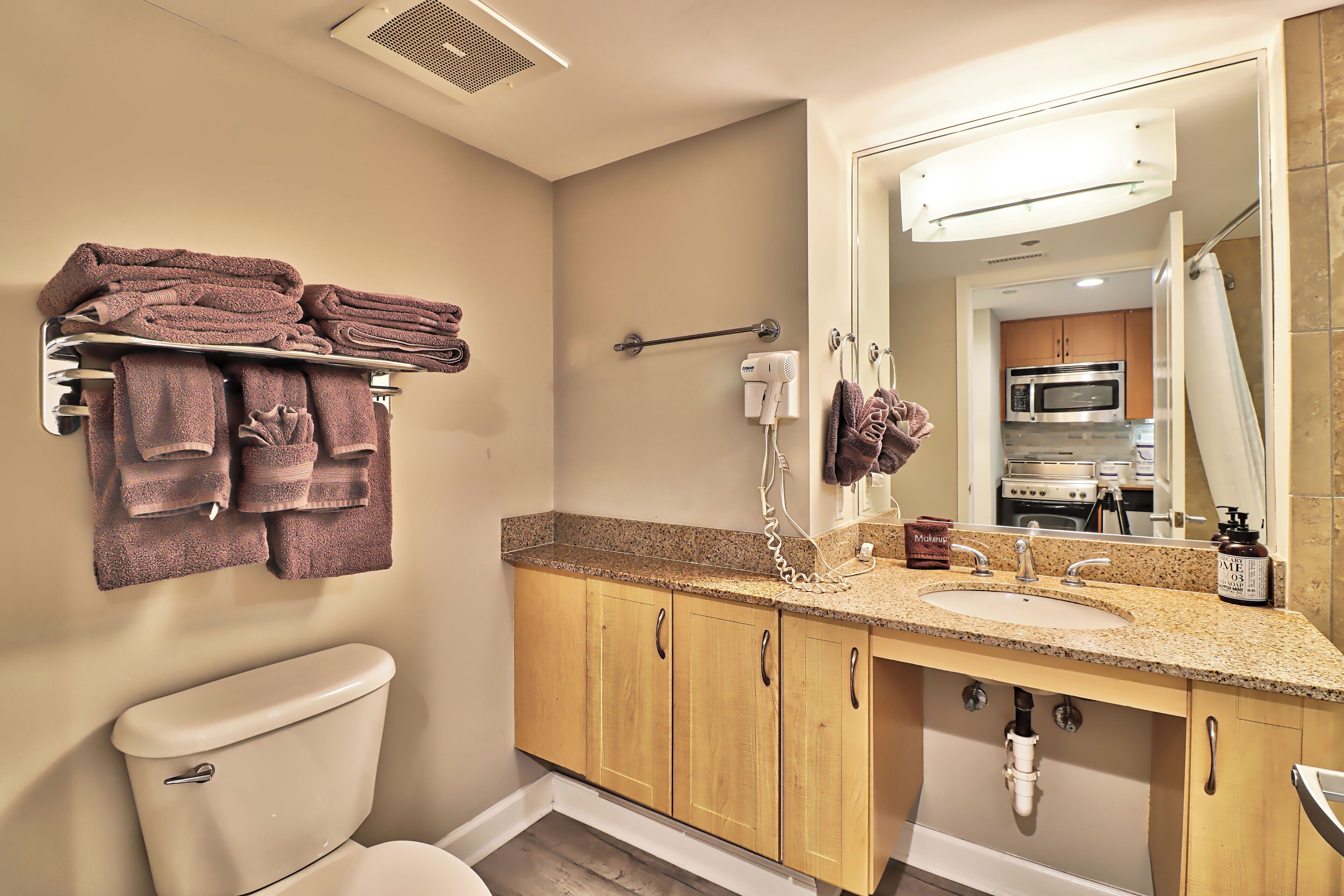 A bathroom with a toilet, sink, and mirror. There are towels on a rack and a hairdryer on the wall.