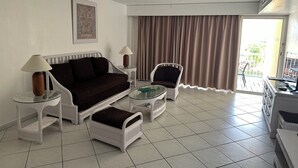Ein Hotelzimmer mit einem dunkelbraunen Sofa, weißen Sesseln, einem Glastisch und einem Deckenventilator.