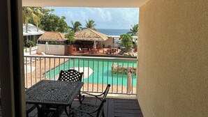 Ein Balkon mit Blick auf ein Schwimmbad, Sitzgelegenheiten im Freien und ein Gebäude mit einem Ziegeldach.