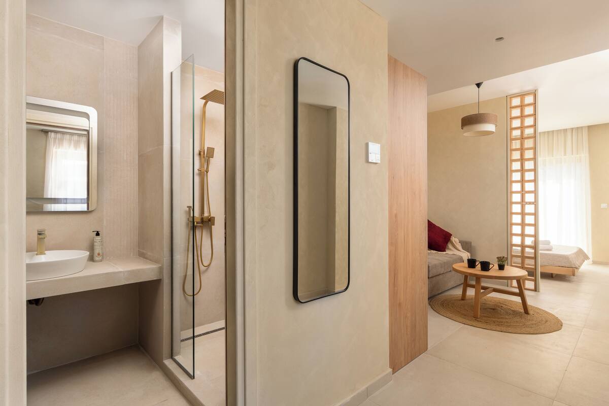 A modern bathroom with a glass shower, a sink, and a mirror. There is a wooden floor and a small round table with a plant.