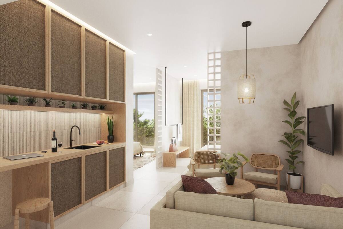 A modern living room with a sofa, a coffee table, and a TV mounted on the wall. There is a kitchen area with a sink and a dining table.