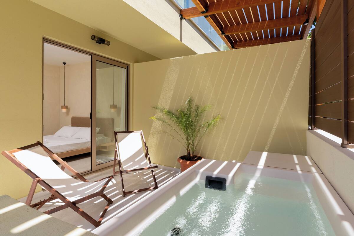 A small outdoor area with a hot tub, a lounge chair, a potted plant, and a sliding glass door leading to a bedroom.