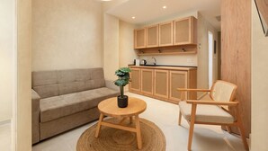 A compact living space with a sofa, a round wooden table with a potted plant, and a wooden chair. - Açai Plant based Hotel (Rhodes)