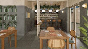 A dining area with a long table, chairs, and hanging plants. There is a bar area with shelves and bottles in the background. - Açai Plant based Hotel (Rhodes)