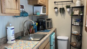 A compact kitchen with wooden cabinets, a microwave, a coffee maker, and a trash bin. -  Tiny Cabin in the Laurels, with queen bed & queen sofa bed in wooded setting. (Marion)