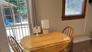 A wooden dining table with two chairs, a lamp, and a small white cabinet. -  Tiny Cabin in the Laurels, with queen bed & queen sofa bed in wooded setting. (Marion)