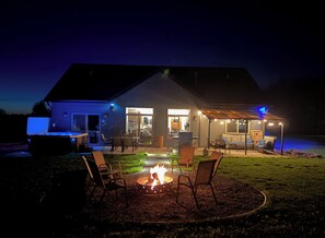 A house with an outdoor patio area featuring a fire pit, seating, and a covered section with string lights.
