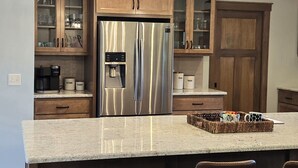 Una cocina con refrigerador de acero inoxidable, gabinetes de madera, encimera de mármol y una lámpara colgante.
