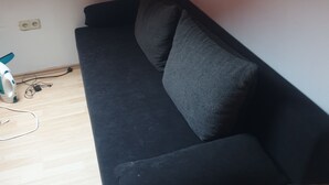 A black sofa in a room with a wooden floor, a white wall, and a red light fixture. - Beautiful apartment in central Ingoöstadt (Ingolstadt)