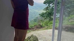 Uma pessoa parada perto de uma janela com vista para uma paisagem verde.