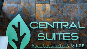 A reception desk with a stone wall background and a logo for Central Suites. - Central Suites by H&R (Villeta)