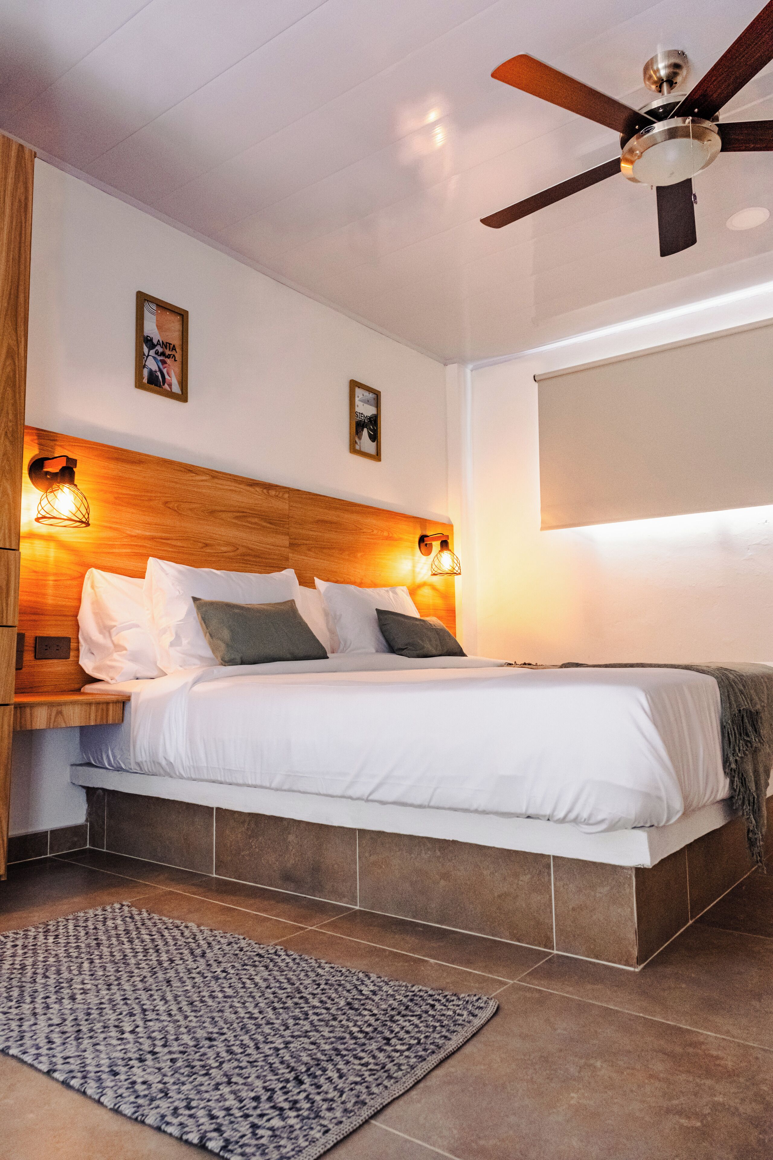 A bedroom with a wooden headboard, a ceiling fan, and a bed with white bedding.