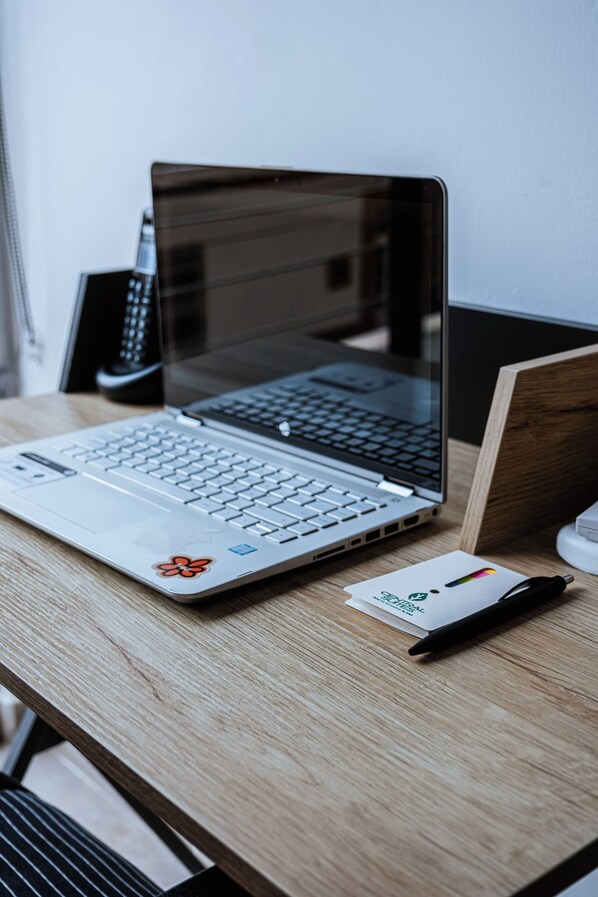 A laptop on a wooden desk with a keyboard, a mouse, and a pen. - Central Suites by H&R (Villeta)