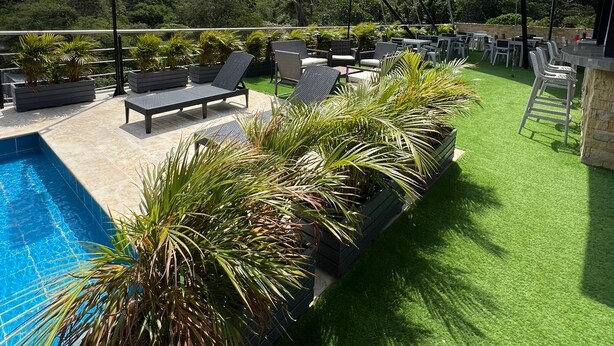 A rooftop pool area with lounge chairs, artificial grass, and a view of the mountains. - Central Suites by H&R (Villeta)