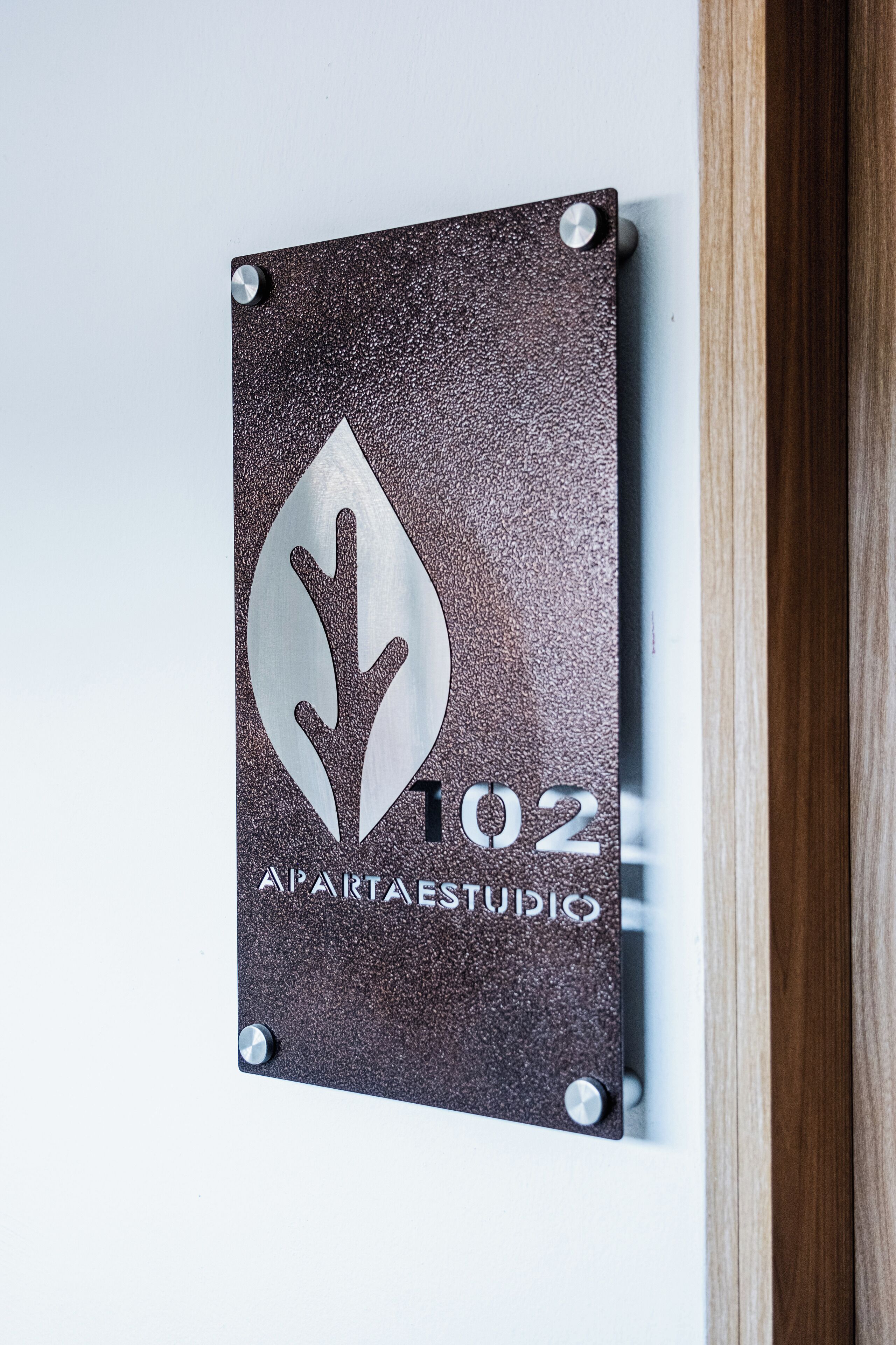 En skylt med ett lövmönster och texten ”102 APARTAESTUDIO”, vilket anger att det är en lägenhet av typen studio.