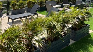 An outdoor seating area with lounge chairs and tables, surrounded by planters and street lamps, overlooking a lush landscape with mountains in the distance. - Central Suites by H&R (Villeta)