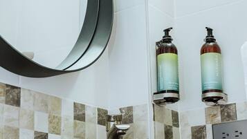 A bathroom with a black sink, a round mirror, and two bottles of shampoo on the wall.
