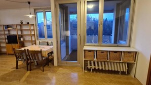 Ein gemütliches Wohnzimmer mit einem Esstisch, Stühlen, einem Bücherregal und Blick durch große Fenster.