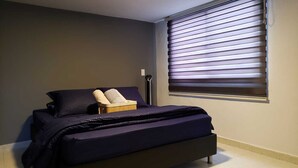 A bedroom with a bed, a chair, a bedside table, and a window with blinds. - 2 bedroom apartment in the best area of Laureles. A/C. (Medellín)