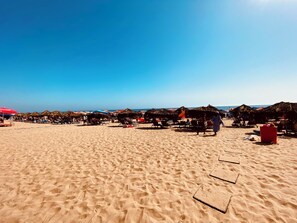 A beach with thatched-roof huts and sun loungers.