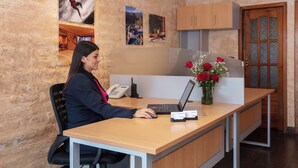 A reception desk with a laptop, phone, and a vase with red flowers. There are wooden cabinets and a door in the background. - Casa del Balcon (Baños de Agua Santa)