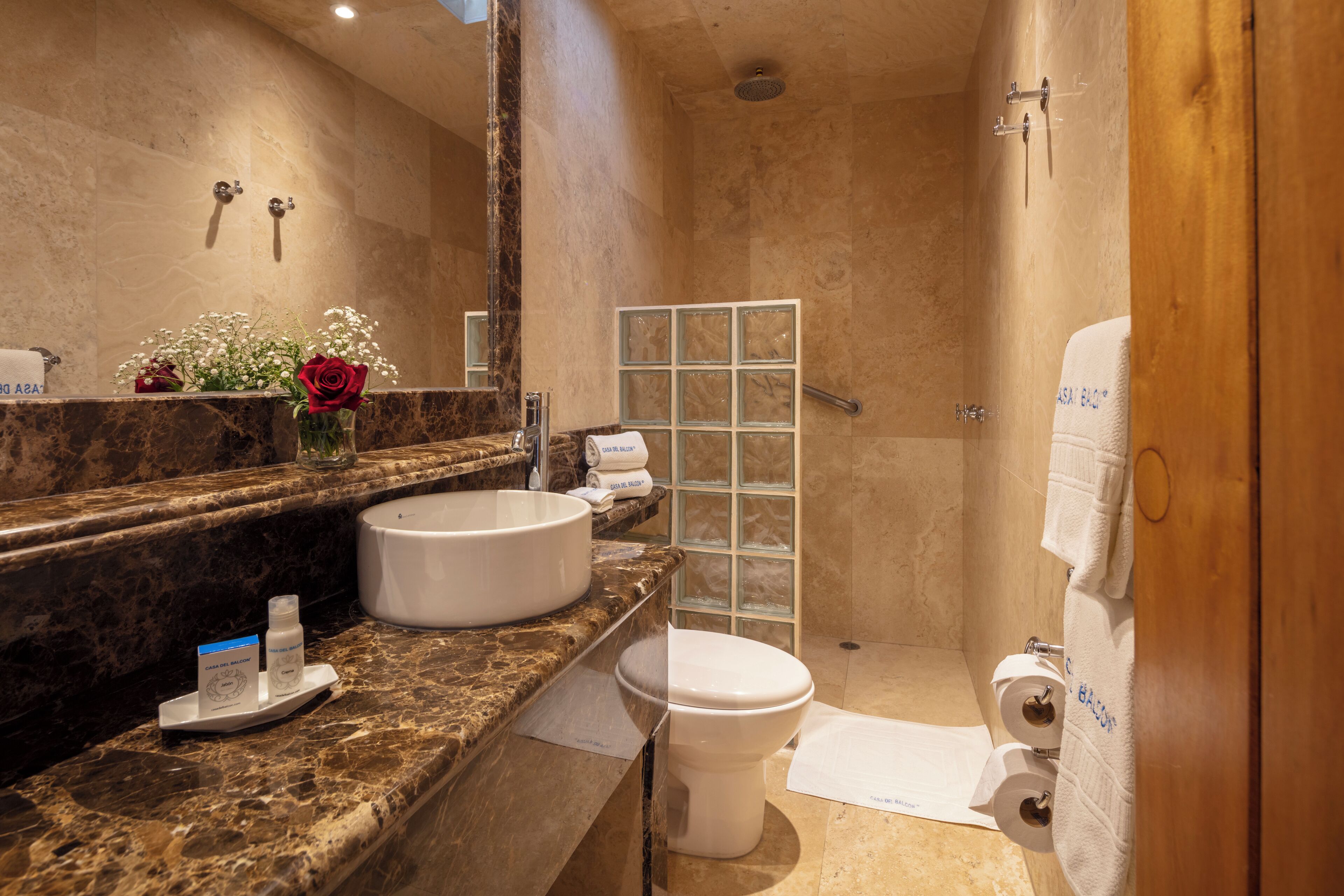 A bathroom with a marble countertop, a white sink, a toilet, and a glass shower enclosure.