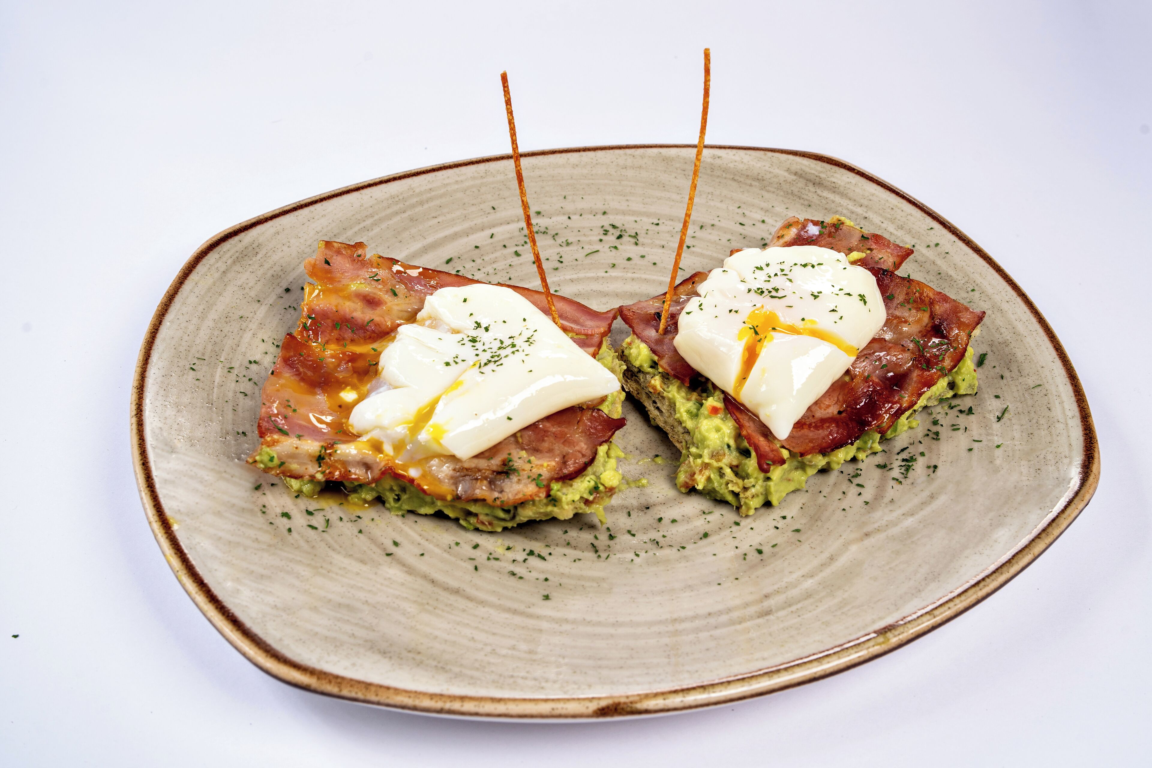 A plate with two pieces of food, each topped with a poached egg and bacon, garnished with herbs.