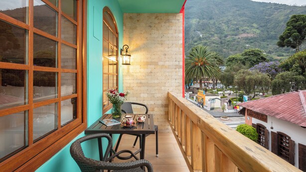 A balcony with a table, chairs, and a view of a mountainous landscape. - Casa del Balcon (Baños de Agua Santa)