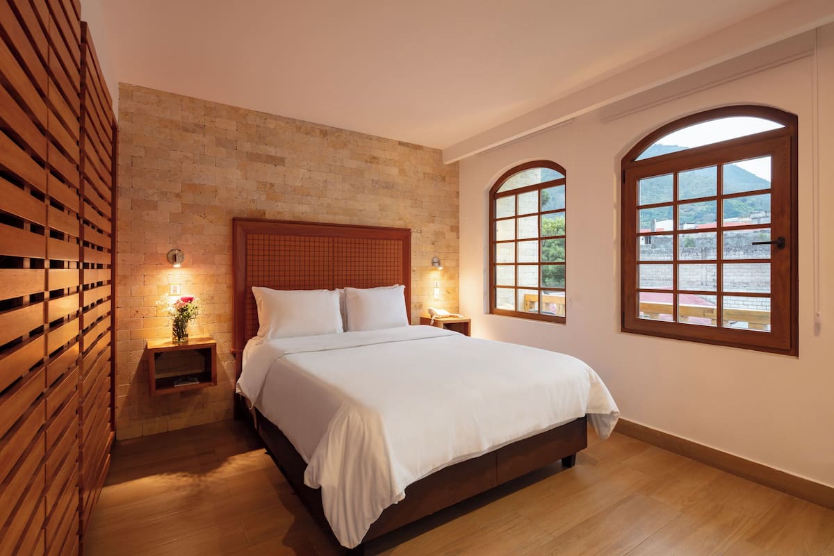 A bedroom with a wooden bed, a brick wall, and two arched windows.