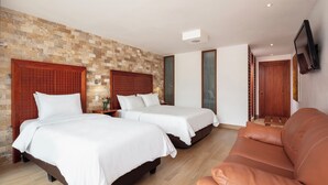 A hotel room with two beds, a brown leather sofa, and a brick-patterned wall. - Casa del Balcon (Baños de Agua Santa)