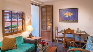 Ein gemütliches Zimmer mit einem grünen Sofa, einem Holzesstisch und einem Stuhl. Auf dem Tisch steht eine Vase mit Blumen, und an der Wand hängt ein gerahmtes Bild.