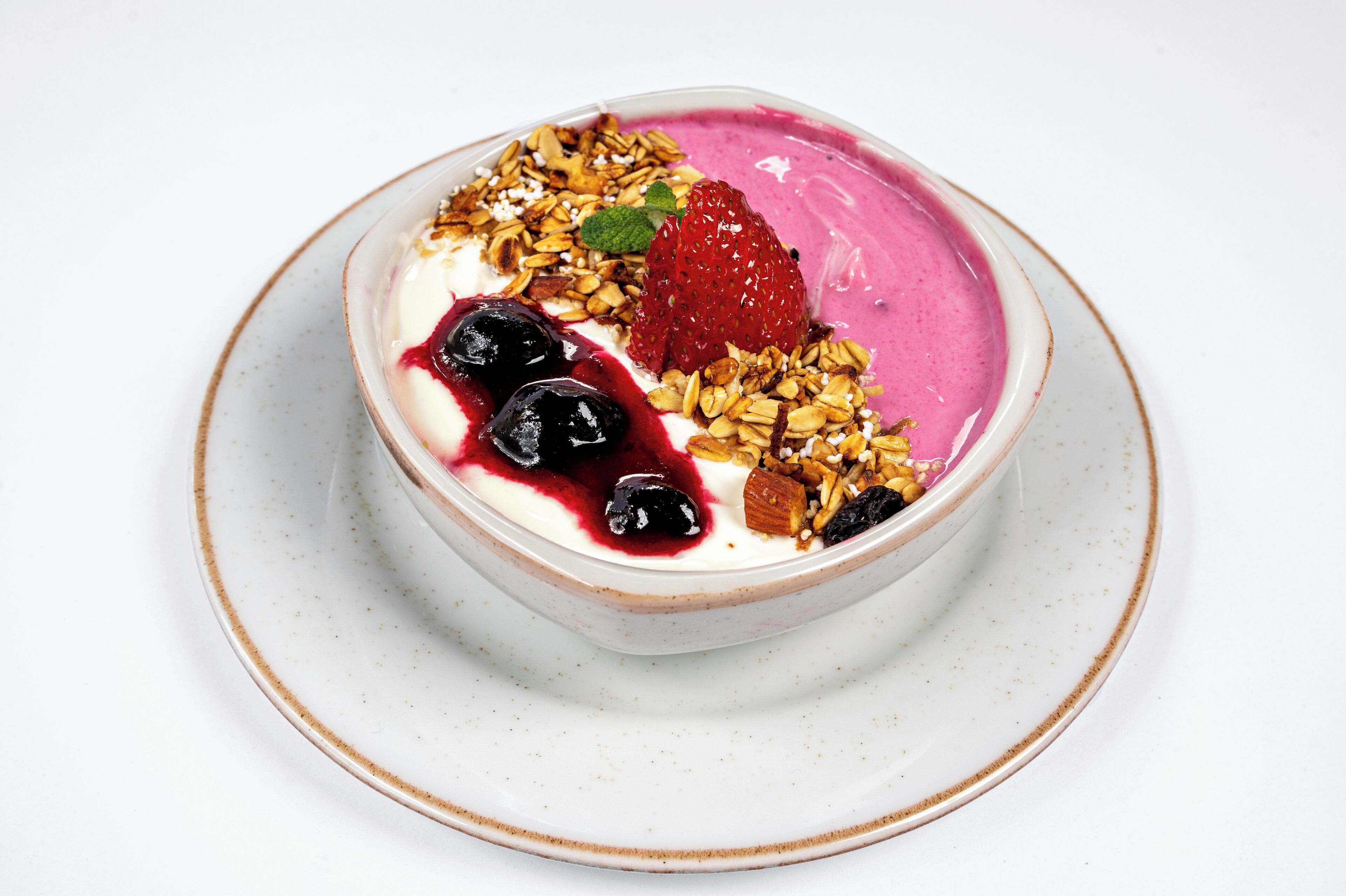 A bowl of yogurt topped with granola, a strawberry, and blueberries.