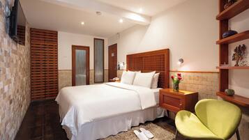 A bedroom with a large bed, a wooden headboard, a nightstand, a green chair, and a brick wall.