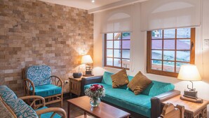 A living room with a brick wall, a teal sofa, a wooden coffee table, and a blue patterned armchair. - Casa del Balcon (Baños de Agua Santa)